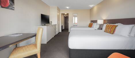 A hotel room with a desk, chair, two beds, a television, and a painting on the wall.