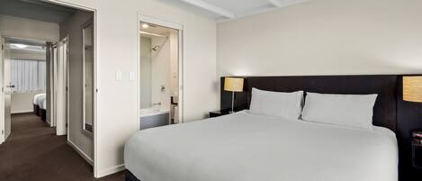 A hotel room with a large bed, a bedside table, a lamp, and a bathroom visible through an open door.
