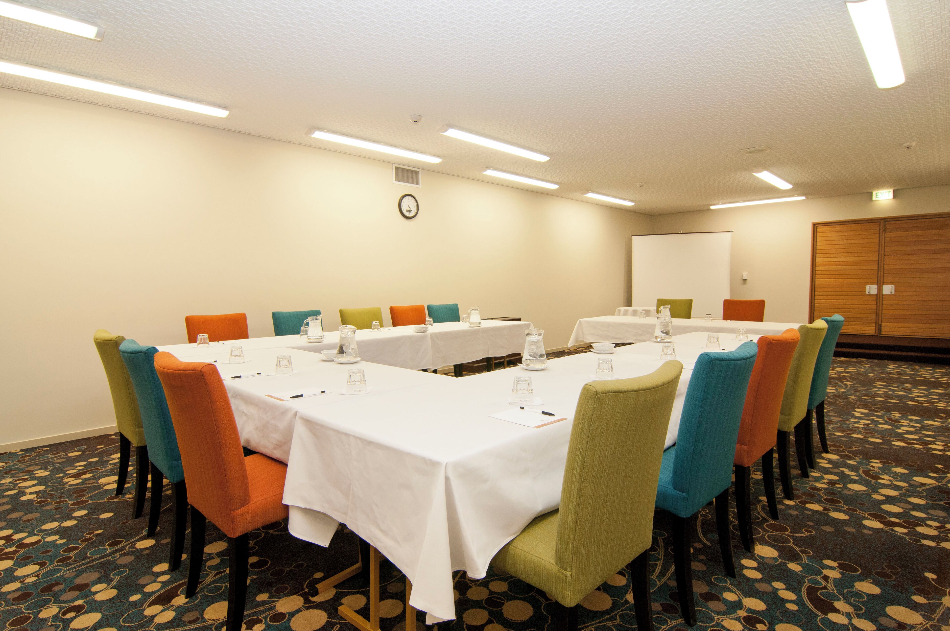 A conference room with white tables, colorful chairs, and a clock on the wall.