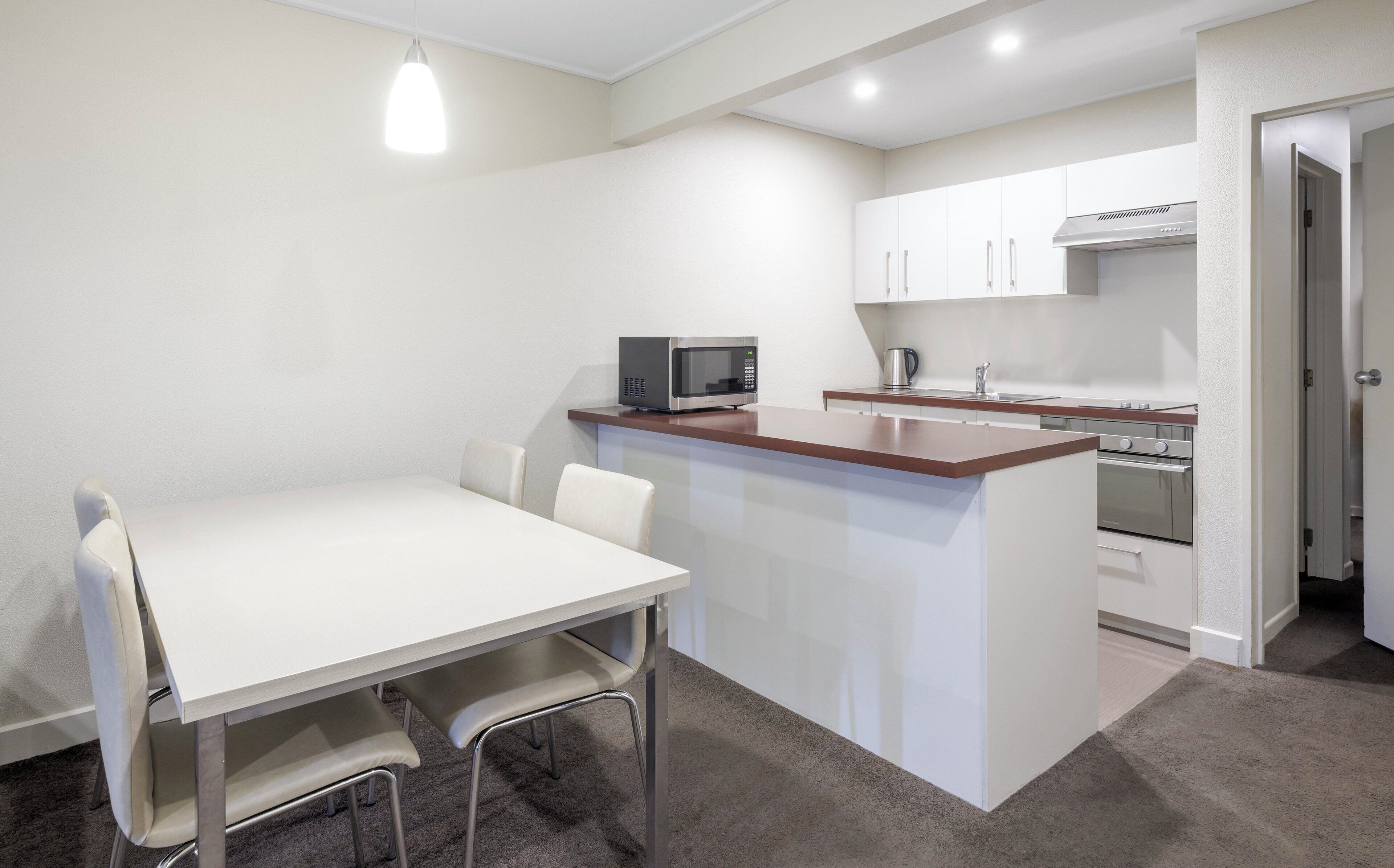 A compact kitchen with a microwave, stove, and sink. There is a dining area with a table and chairs.