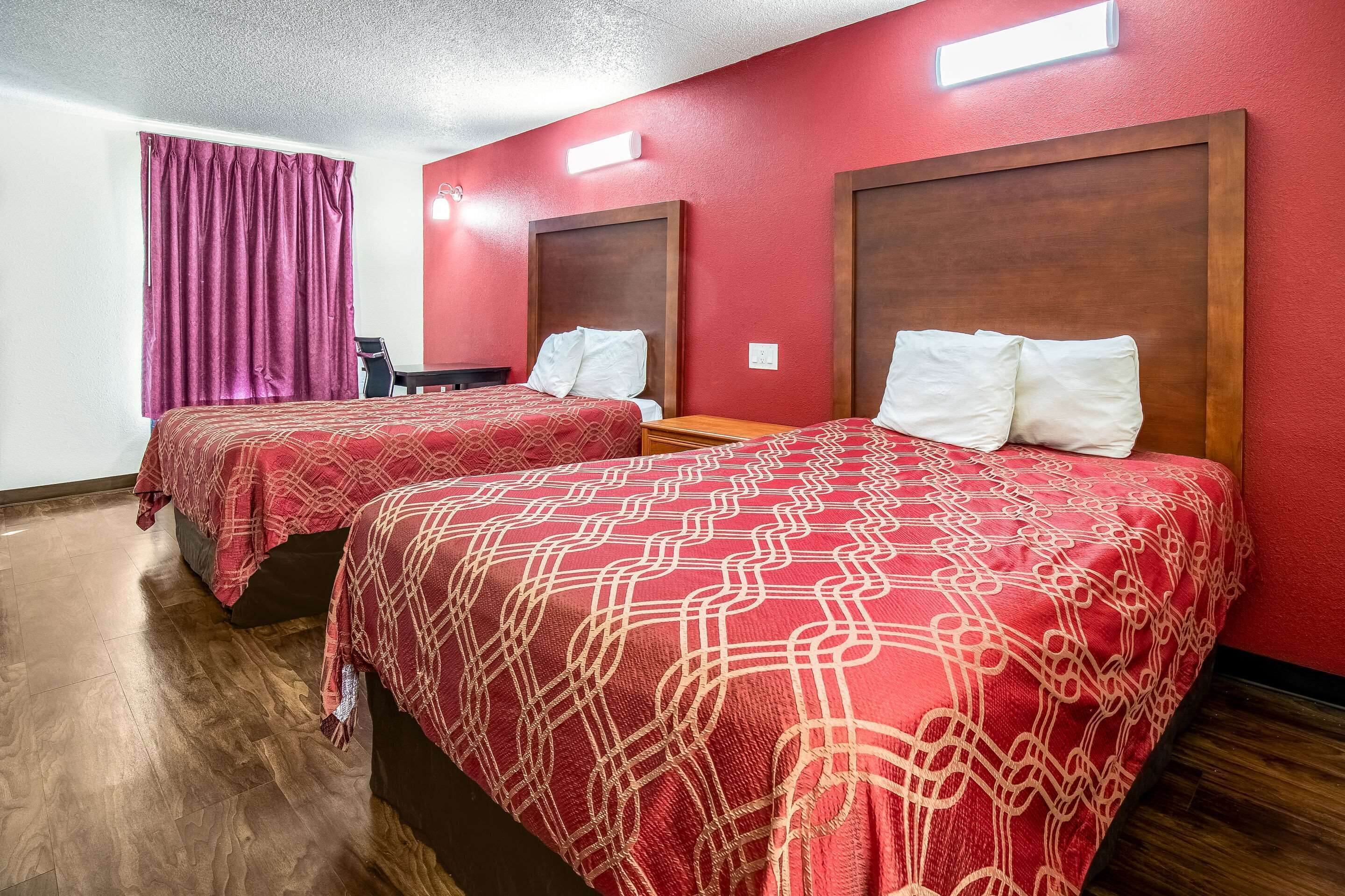 A hotel room with two beds, each with a red patterned bedspread, wooden headboards, and white pillows.