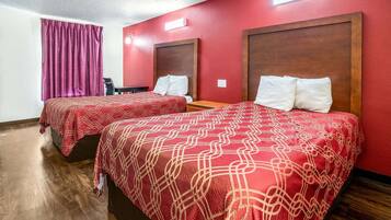 A hotel room with two beds, each with a red patterned bedspread, wooden headboards, and white pillows.