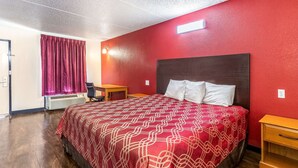 A hotel room with a large bed, a wooden nightstand, a desk, and a red wall. - Econo Lodge Knoxville West - Turkey Creek (Knoxville)