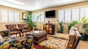 A living room with floral-patterned sofas, a leather ottoman, a TV mounted on the wall, and potted plants. - Econo Lodge Knoxville West - Turkey Creek (Knoxville)