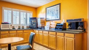 A hotel kitchen with wooden cabinets, a microwave, a coffee machine, and a dining area with a chair and table. - Econo Lodge Knoxville West - Turkey Creek (Knoxville)