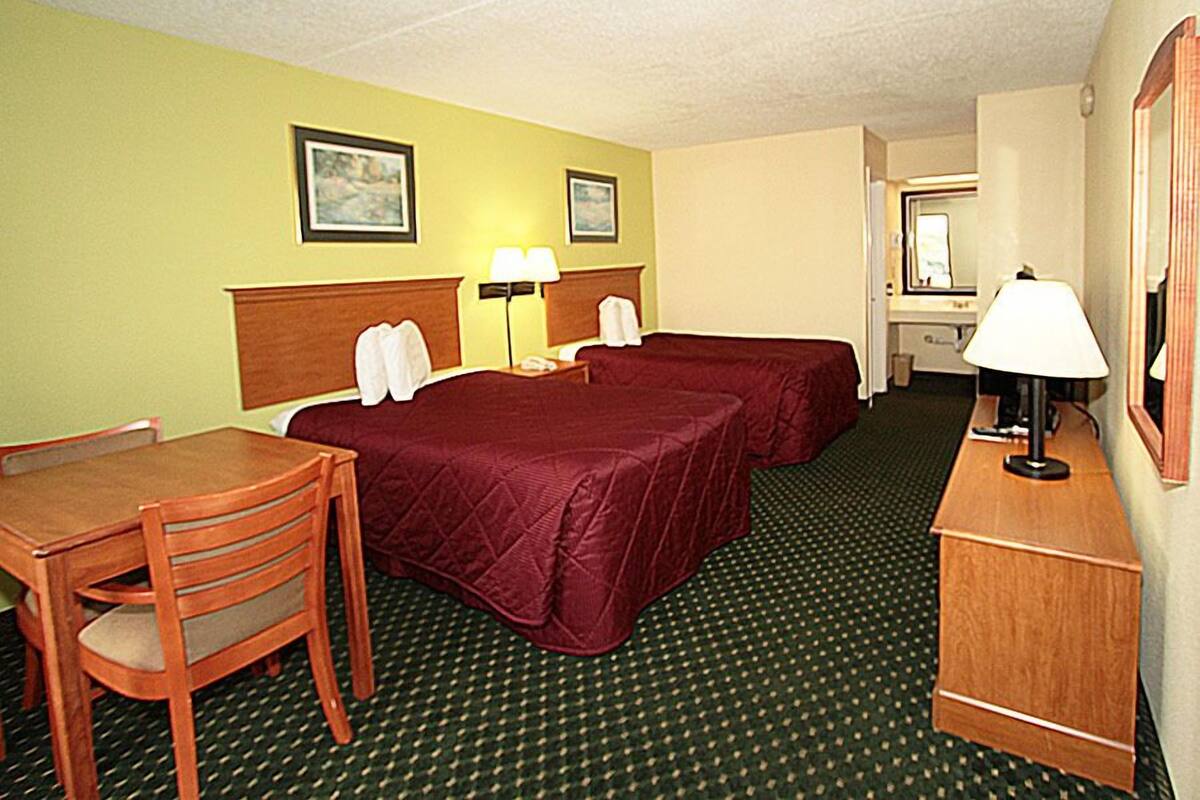 A hotel room with two beds, a desk, a chair, a lamp, and a mirror.