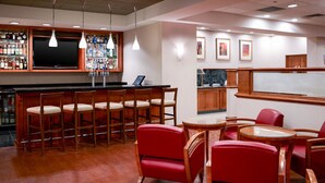 A bar area with wooden bar stools, a television, and a liquor display. There are red chairs and a small table with a glass top. - Clarion Hotel Portland Airport ME (Portland)
