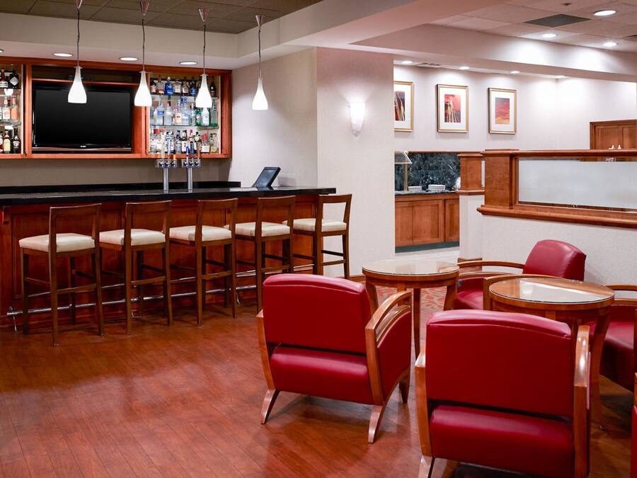 A bar area with wooden bar stools, a television, and a liquor display. There are red chairs and a small table with a glass top.