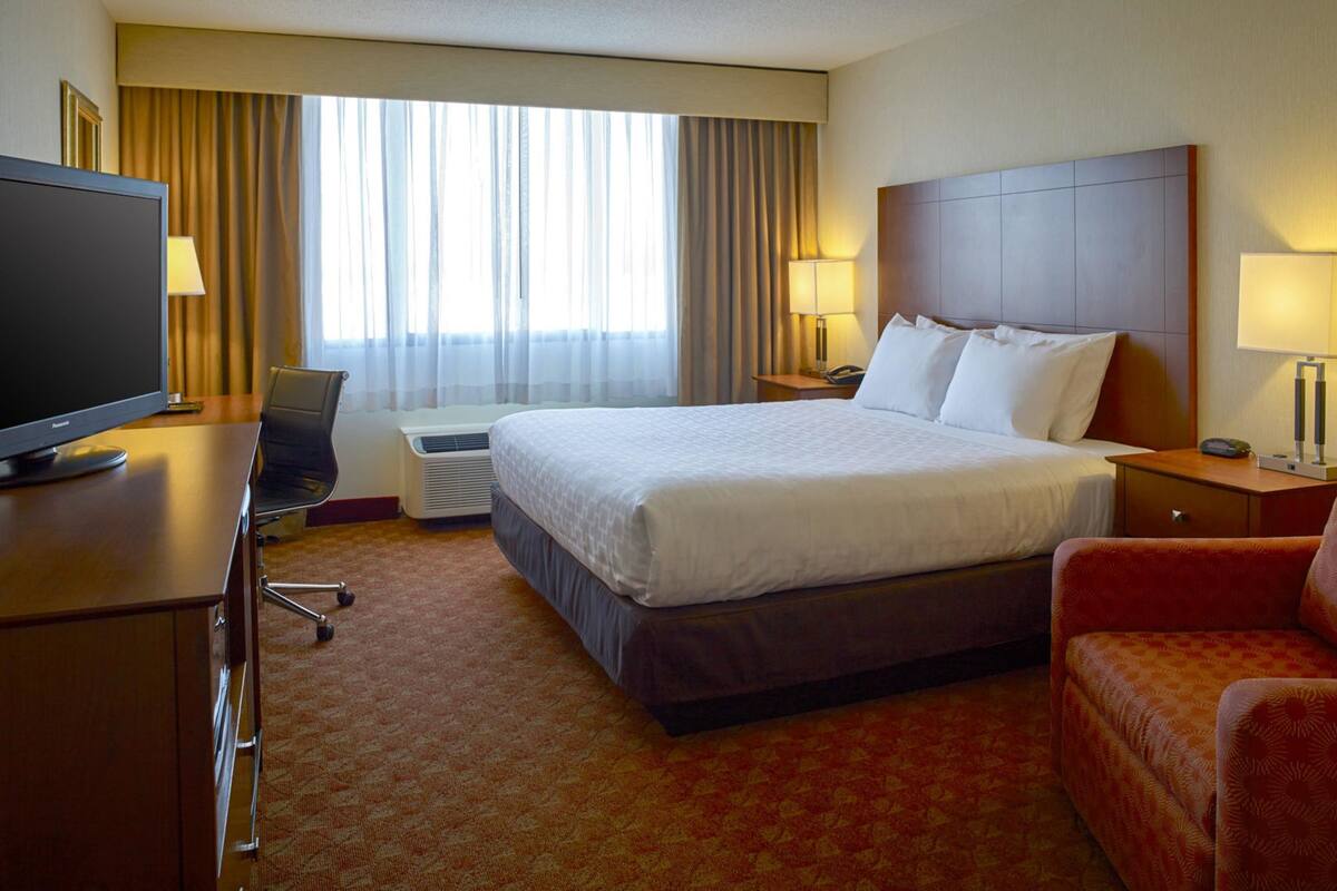 A hotel room with a large bed, a desk with a television, a chair, and a sofa.