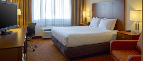 A hotel room with a large bed, a desk with a television, a chair, and a sofa.