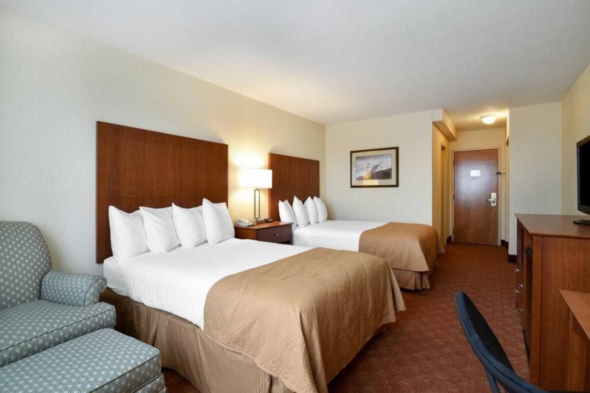 A hotel room with two beds, a desk, a chair, and a television.