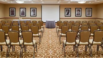 A conference room with rows of chairs, a projector screen, and framed pictures on the walls.