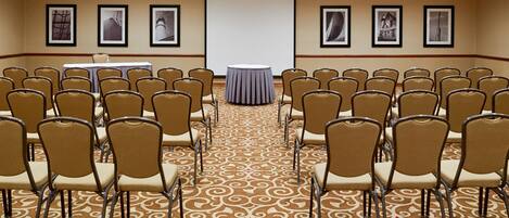 A conference room with rows of chairs, a projector screen, and framed pictures on the walls.