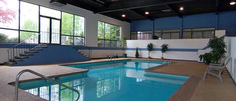 An indoor swimming pool with clear blue water, a staircase leading to an upper level, and large windows allowing natural light.