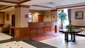 A lobby with a reception desk, a clock, a plant, and a round table. - Clarion Hotel Portland Airport ME (Portland)