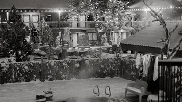 Un espacio exterior cubierto de nieve con un jacuzzi, asientos y un edificio con luces al fondo.