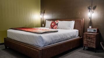 A hotel room with a large bed, two wall sconces, a nightstand with a radio, and a carpeted floor.