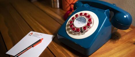 A blue rotary phone on a wooden table with a red pen and a piece of paper.
