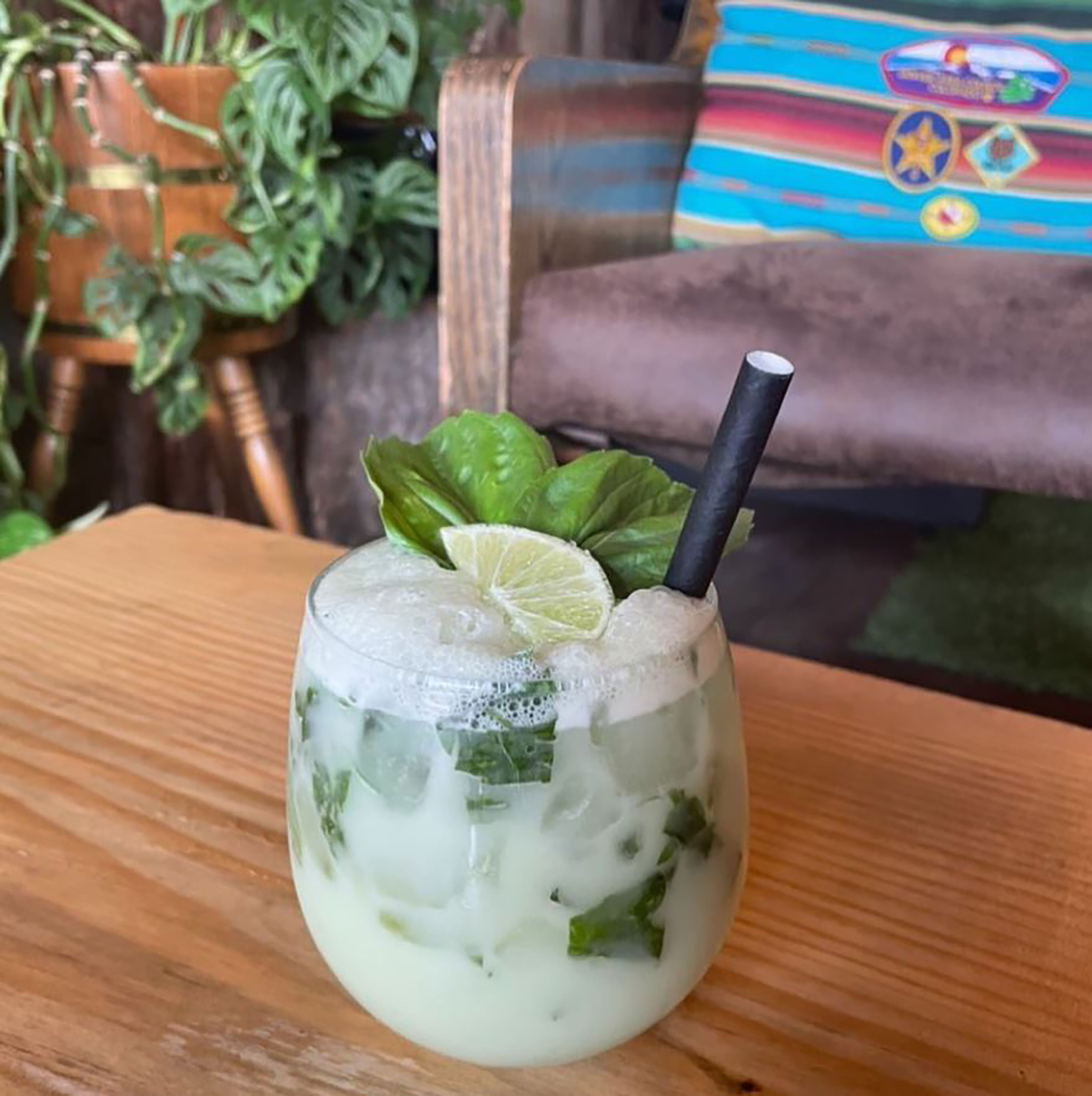 A glass of a light-colored beverage with ice, garnished with a lime slice and a black straw, on a wooden table.