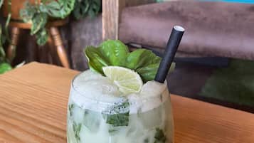 A glass of a light-colored beverage with ice, garnished with a lime slice and a black straw, on a wooden table.