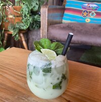 A glass of a light-colored beverage with ice, garnished with a lime slice and a black straw, on a wooden table.