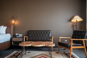 A hotel room with a bed, a dark brown sofa, a wooden coffee table, a wooden armchair, a lamp, and a radio on a nightstand.