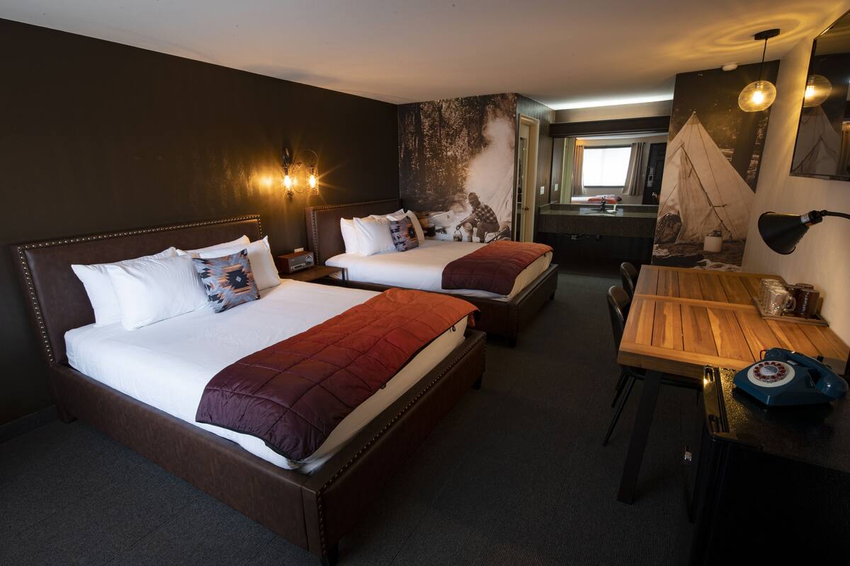 Habitación de hotel con dos camas, un escritorio de madera y un ventanal grande.