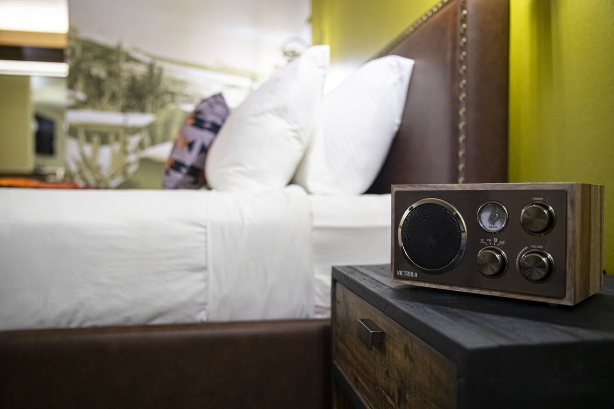Una radio sobre una mesita de noche de madera en una habitación de hotel, con una cama al fondo.