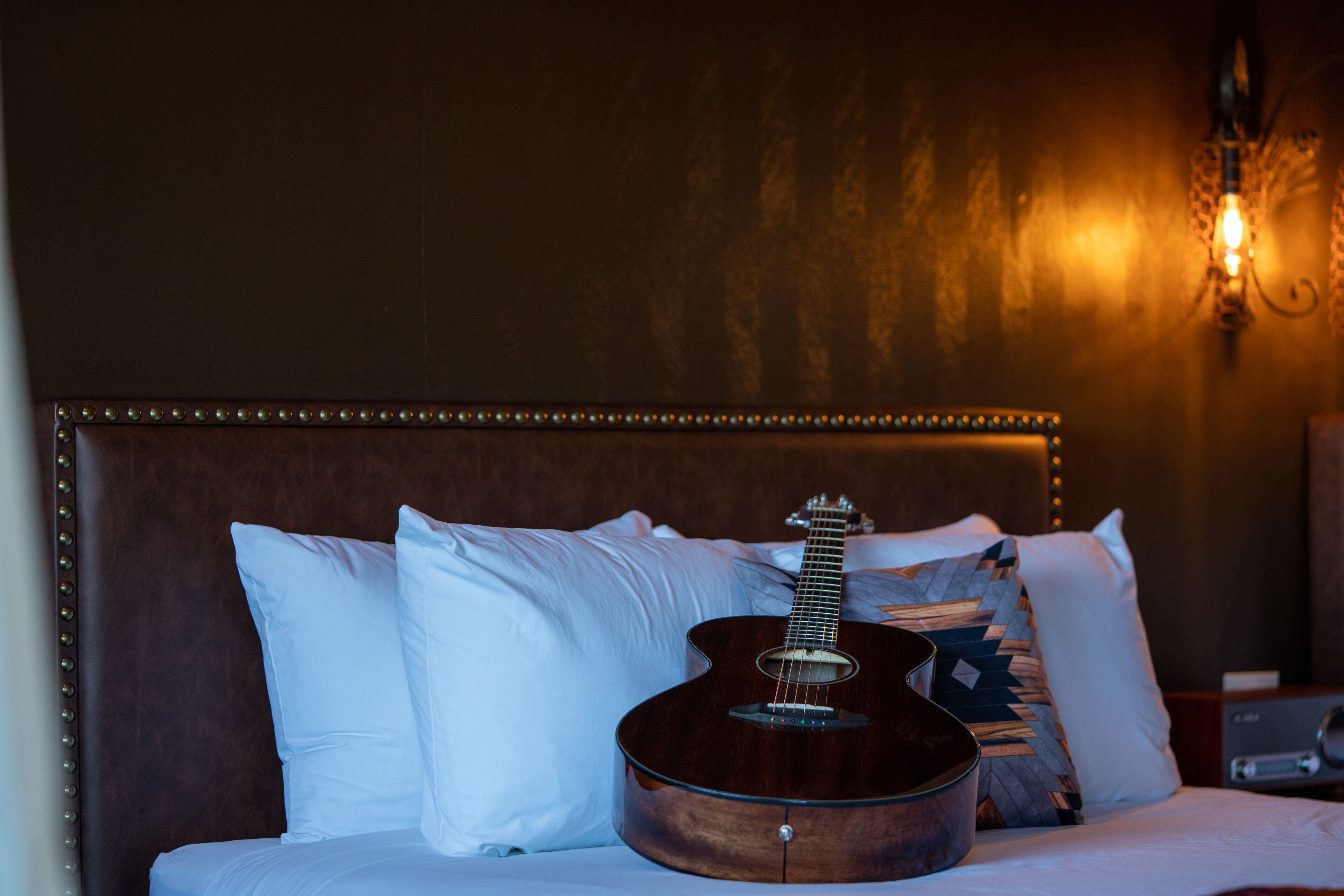A bed with a guitar, pillows, and a wall-mounted light fixture.