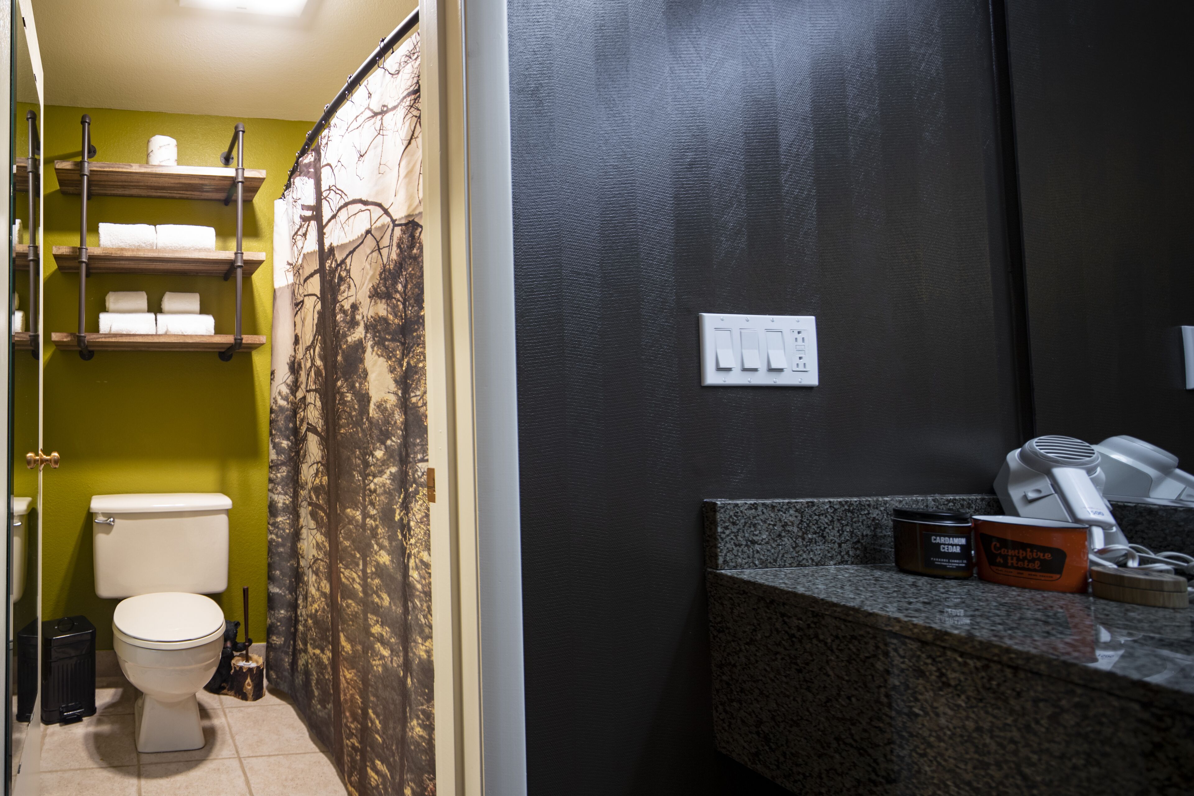 Un bagno con il water, mensole con asciugamani, un lavandino con articoli da toilette e una tenda della doccia con motivo alberi.