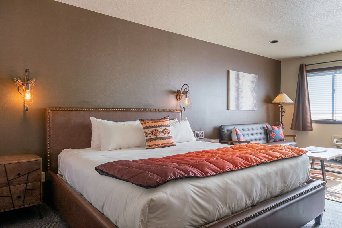 Habitación de hotel con una cama grande, lámparas de noche, un escritorio y una ventana con persianas.
