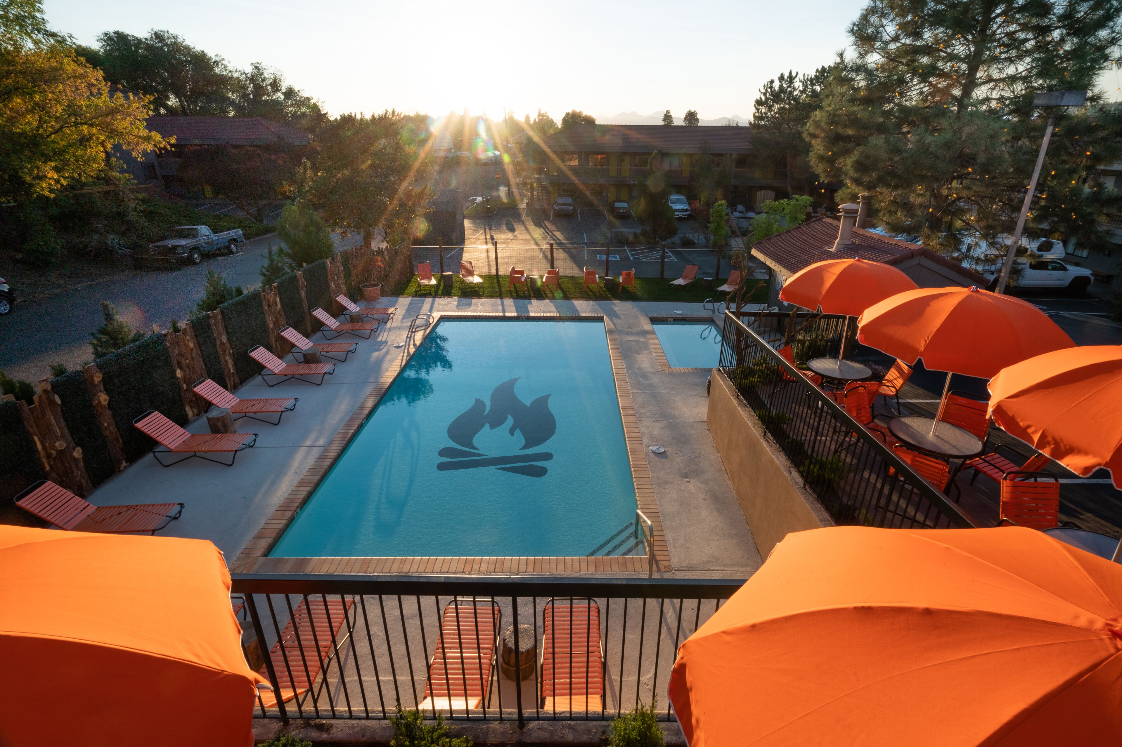 A swimming pool with lounge chairs and umbrellas, surrounded by a fence and trees.