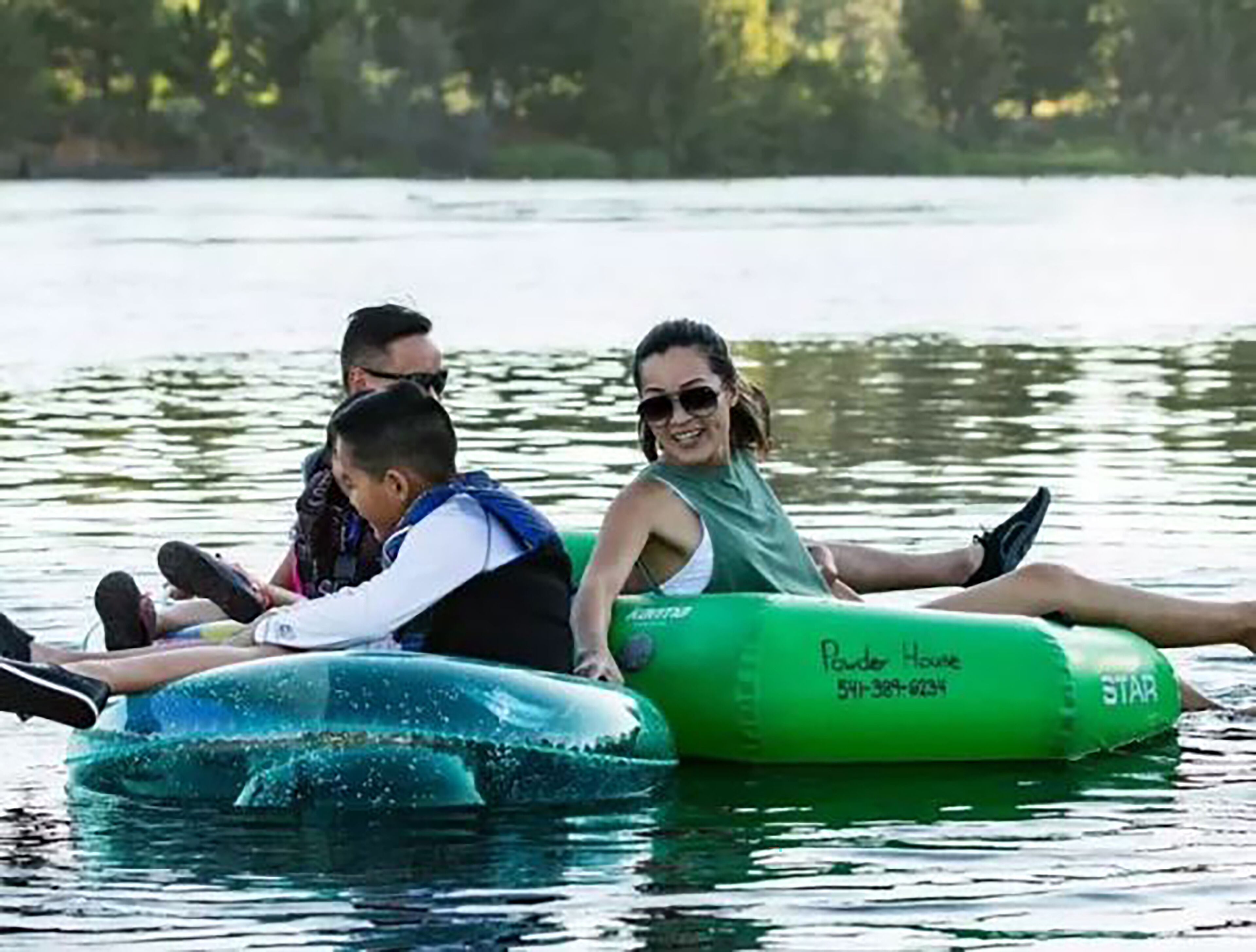 Three people on a green inflatable raft with 'Powder House' and a phone number on it.