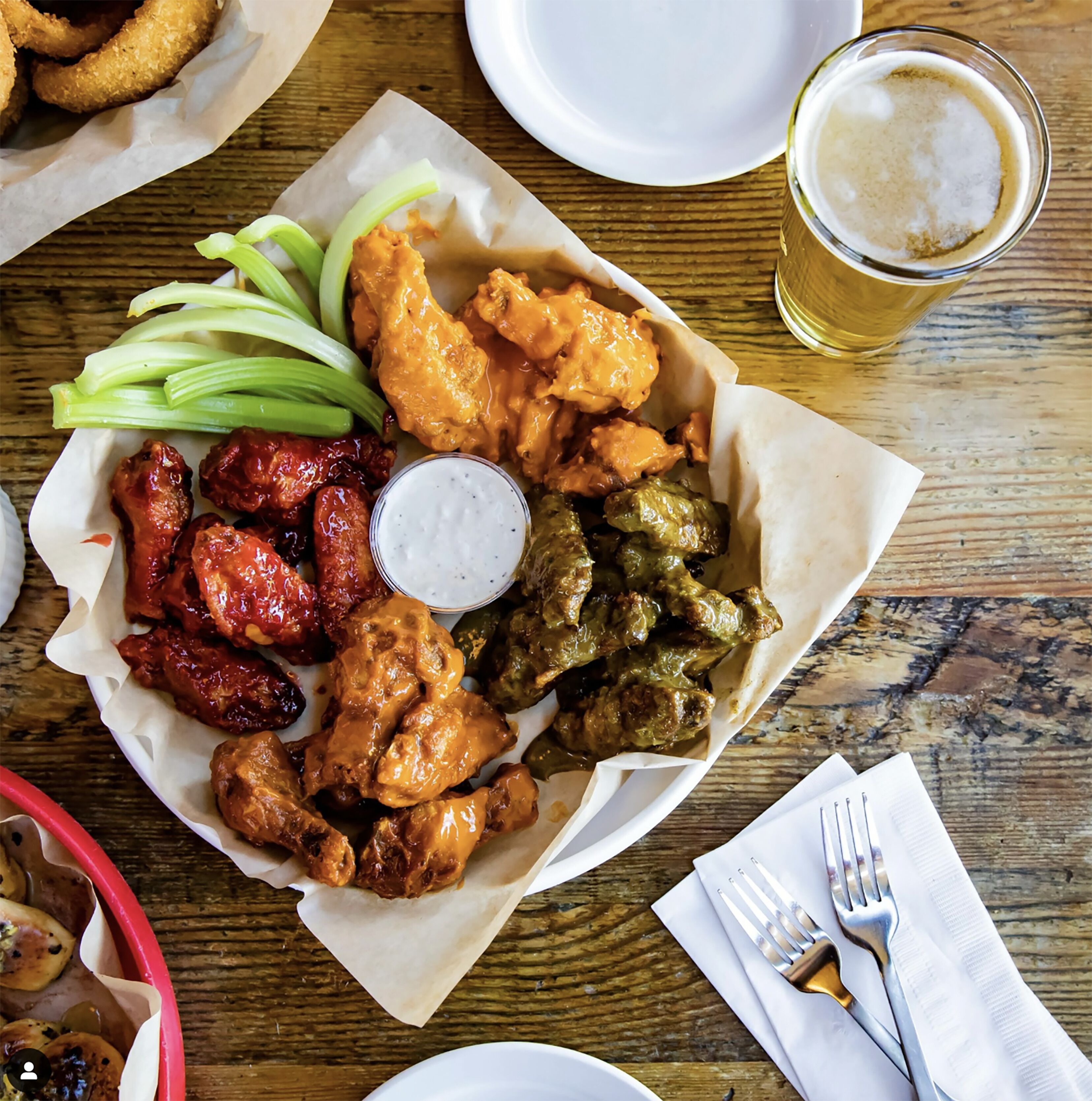 A table with a basket of fried chicken wings, buffalo wings, and green beans, accompanied by a small bowl of dipping sauce.