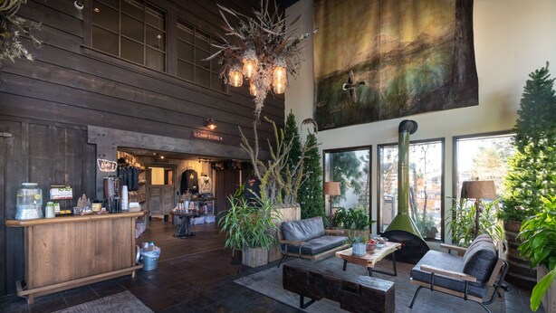 A spacious lobby with a wooden reception desk, comfortable seating area, and large windows offering views of the outdoors. - Campfire Hotel (Bend)