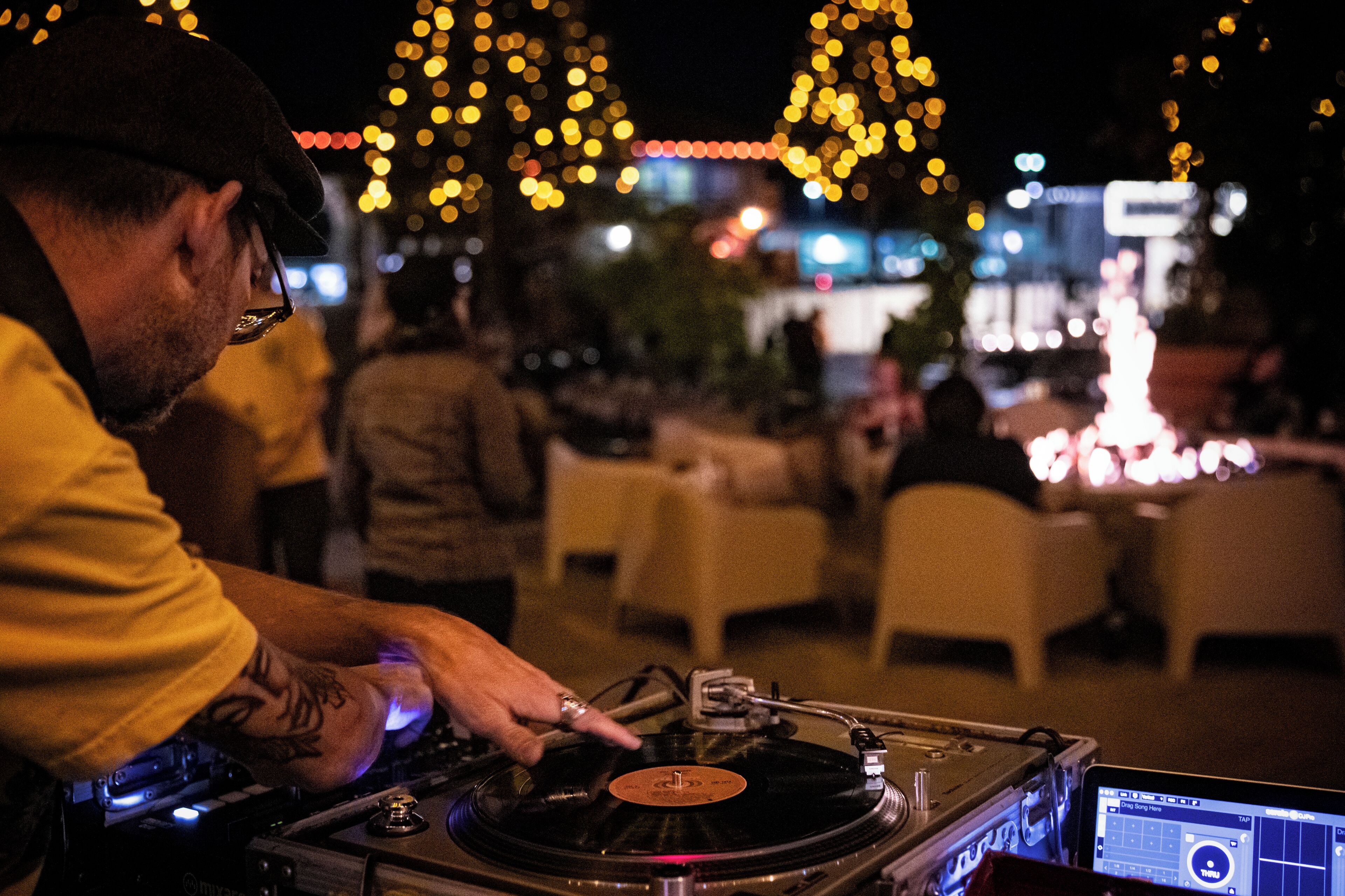 A DJ performing at an outdoor event with tables and chairs in the background.