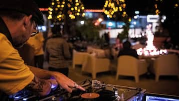 A DJ performing at an outdoor event with tables and chairs in the background.