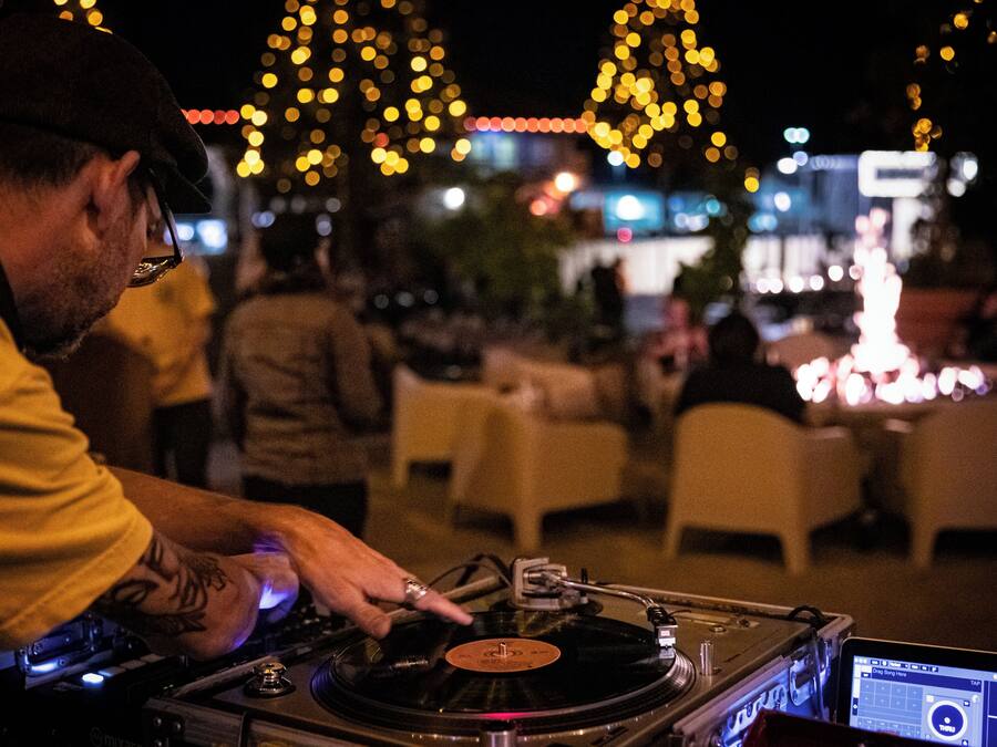 A DJ performing at an outdoor event with tables and chairs in the background.
