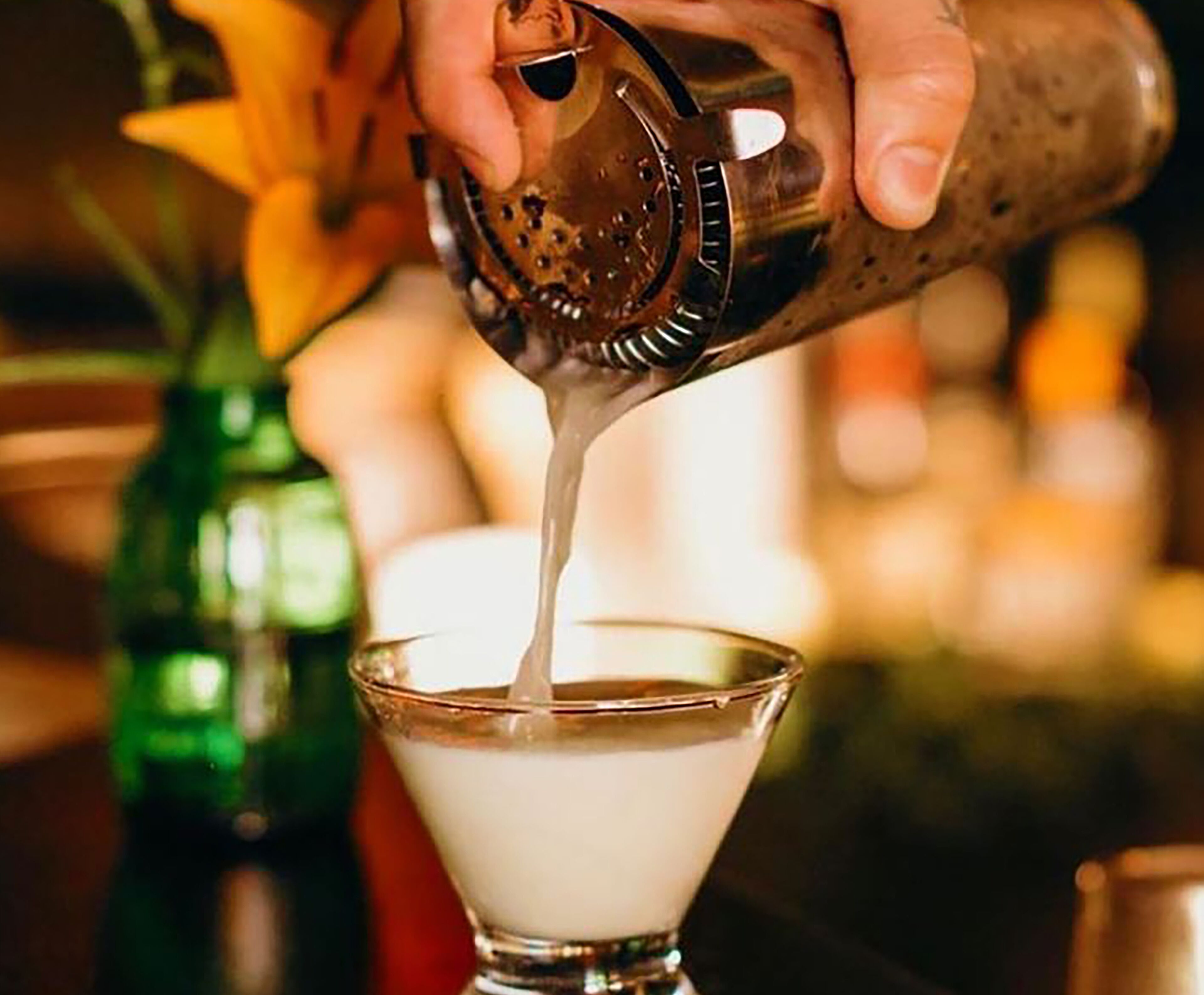 A person pouring a liquid into a martini glass.