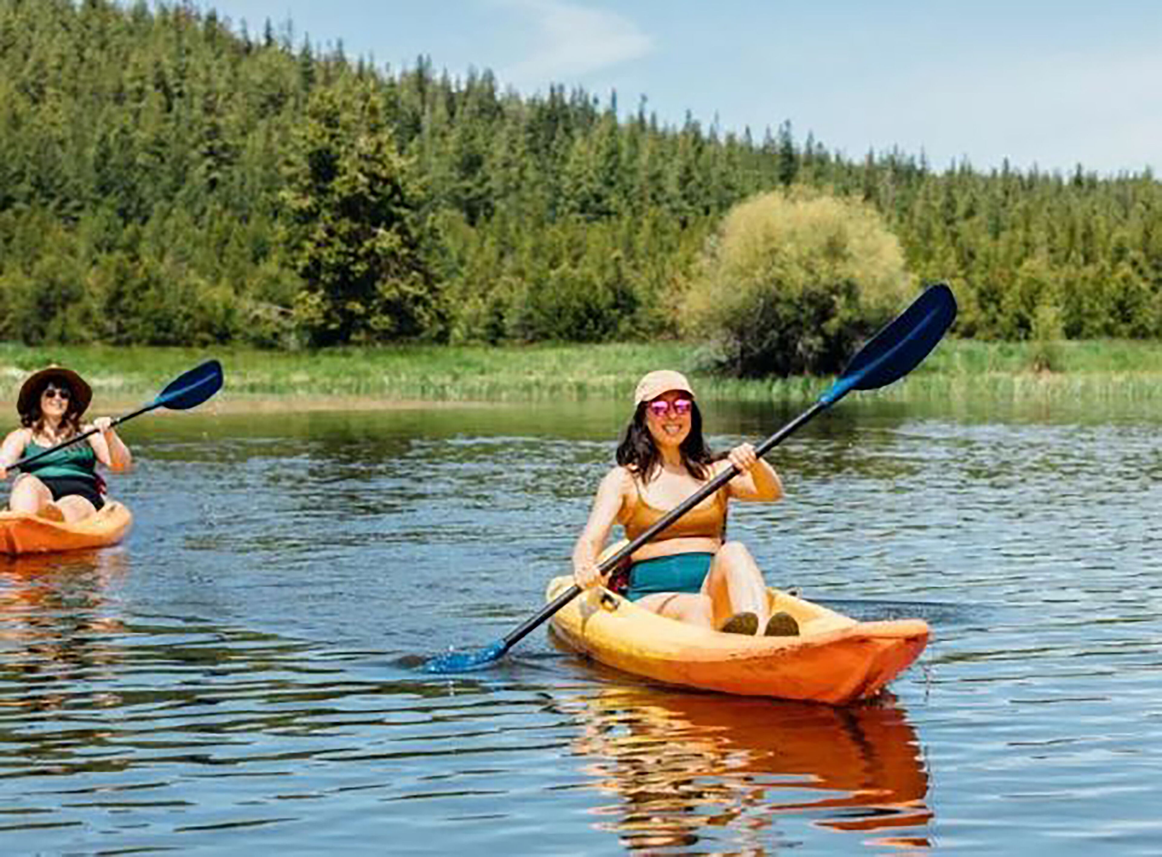 Two people kayaking on a calm river surrounded by dense forest.