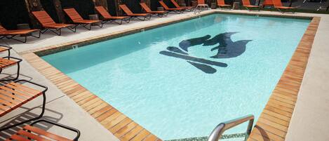 A rectangular swimming pool with a wooden deck and orange lounge chairs.