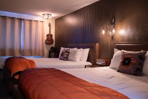 Hotellihuone, jossa on kaksi sänkyä, kitara ja seinään kiinnitetty valaisin.
