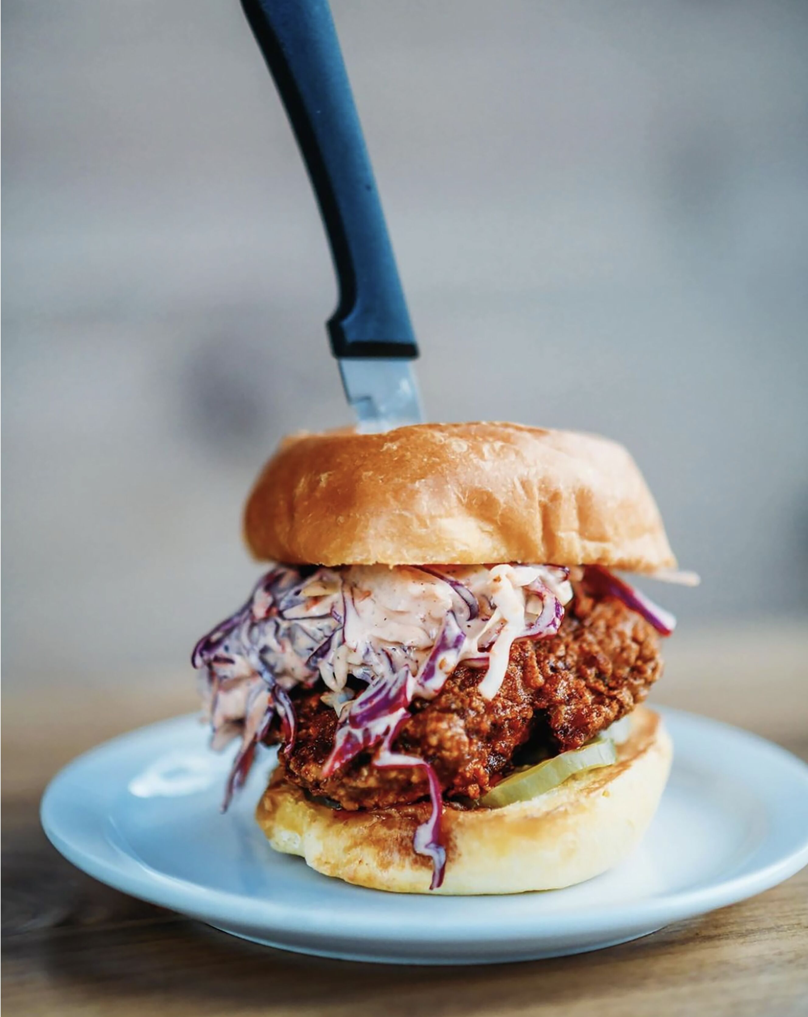 A sandwich with a bun, meat, and coleslaw on a plate.
