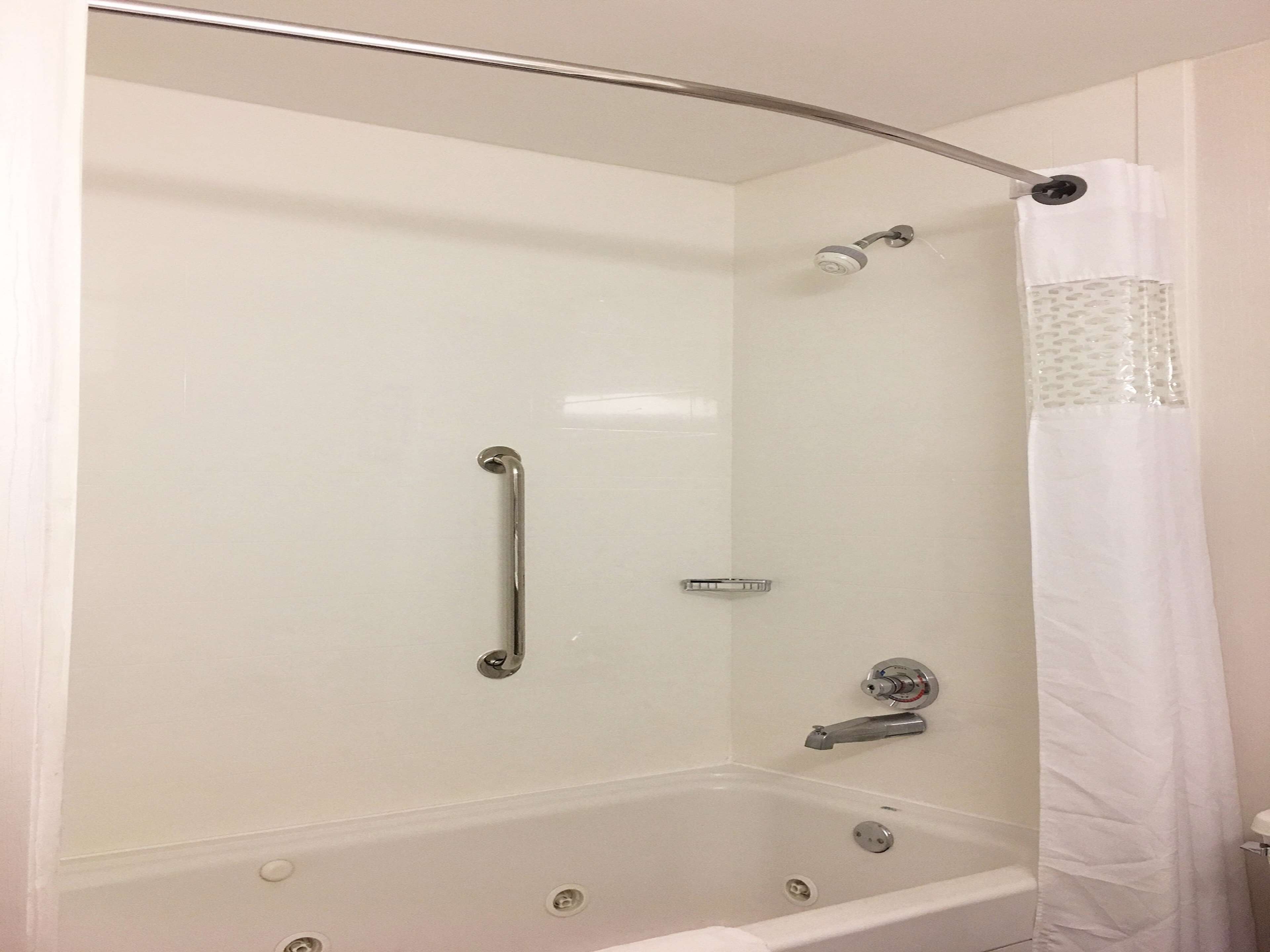 A walk-in shower with a glass door, a handheld showerhead, a handheld shower control, and a white shower curtain.