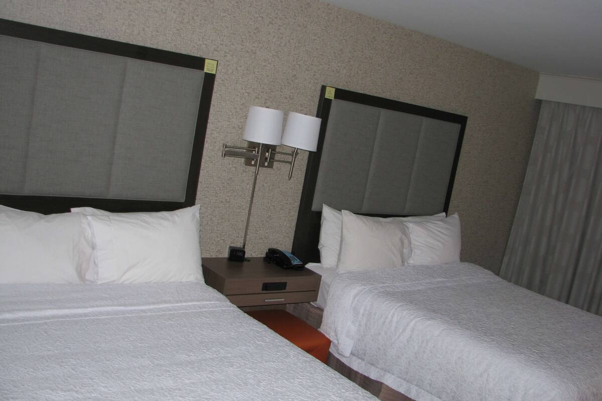 A hotel room with two beds, a nightstand, a lamp, and a telephone.