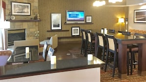 Un vestíbulo de hotel con pared de piedra, chimenea, televisor, cuadros enmarcados, zona de comedor con sillas y mesa, y alfombra estampada.