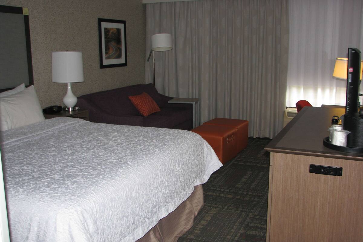 A hotel room with a large bed, a desk, a chair, a sofa, and a window with curtains.