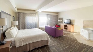 Habitación de hotel con cama, escritorio con televisor, sofá y baño con bañera.