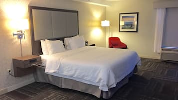 Habitación de hotel con una cama grande, una mesita de noche, una silla roja, una lámpara de pared y un cuadro enmarcado.