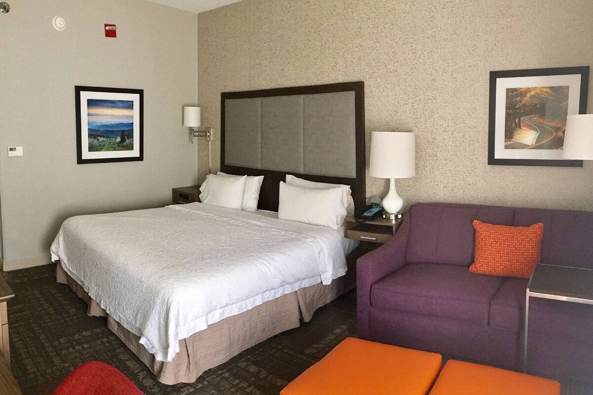 A hotel room with a large bed, a sofa, and a small table with a lamp.